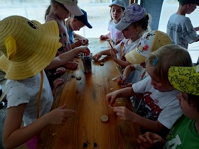 Dzieci siedzą przy stole i ozdabiają flamastrami drewniane magnesy.