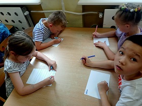 Dwie dziewczynki i dwóch chłopców siedzi przy stoliku i piszę flamastrami po kartce A5.