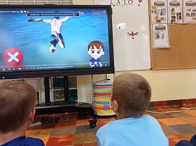 Dwóch chłopców ogląda na monitorze sytuacje, gdy ktoś skacze do basenu. Na ekranie pojawia się czerwony X.