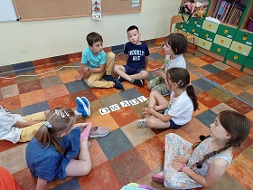 Dzieci siedzą na podłodze i analizują słowo owady ułożone z kartoników z literami.