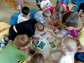Dzieci siedzą na podłodze i wskazują palcami obrazki owadów ułożone w dwóch kółkach sznurka. 