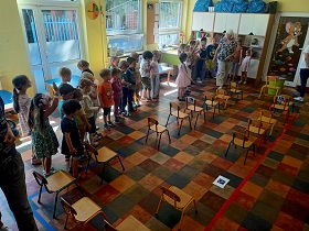 Dzieci stoją w sali, w której ustawione są krzesła na środku sali. Krzesła mają symbolizować siedzenia w tramwaju. Na dwóch krzesełkach i na podłodze znajdują się znaczki mówiące o osobach niepełnosprawnych. 