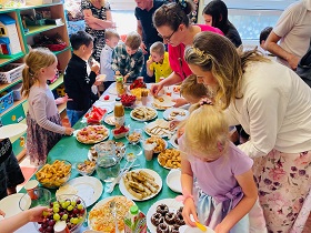 Dzieci i dorośli nakładają sobie smakołyki ze szwedzkiego stołu ze słodkościami. 
