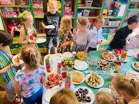 Dzieci nakładają sobie smakołyki ze szwedzkiego stołu ze słodkościami. 