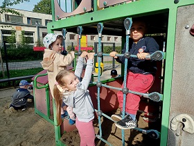 Dwie dziewczynki i chłopiec wspinają się taśmach na placu zabaw. 