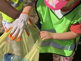 Do żółtego worka dziewczynka wrzuca plastikową butelkę.