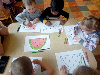 Przy stoliku siedzi piątka dzieci i koloruje prace plastyczną - arbuza. 