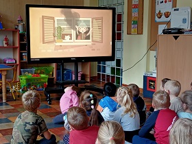 Dzieci siedzą przed monitorem i oglądają filmik instruktażowy jak postępować w przypadku pożaru. 