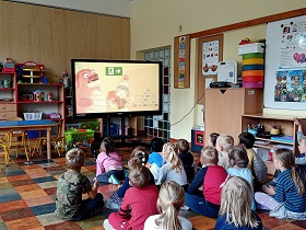 Dzieci siedzą przed monitorem i oglądają filmik instruktażowy jak postępować w przypadku pożaru. 