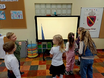 Dzieci stoją przed ekranem monitora i oglądają wyświetlaną prezentacje. 