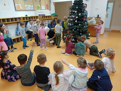 Dzieci i dorośli ubierają choinkę, która stoi na środku szatni. 