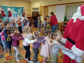 Dzieci wraz z Mikołajem i królową robią pociąg. Trzymają się za ramiona. 