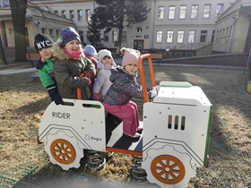 Pięcioro dzieci siedzi w drewnianym aucie w ogrodzie przedszkolnym.