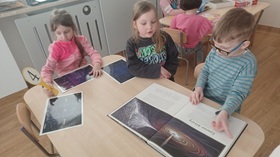 Troje dzieci przy stoliku przegląda książki o tematyce związanej z kosmosem