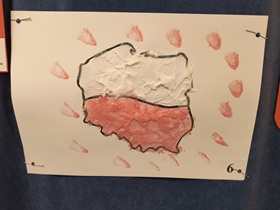 Praca wykonana na białej kartce przedstawiająca kontur Polski, podzielony wszerz na pół. Górna część pomalowana jest na biało, dolna na czerwono. Na około widnieją czerwone plamy, zrobione pędzlem. Praca pomalowana jest puszystymi farbami, wykonanymi z pianki do golenia, farby i kleju.