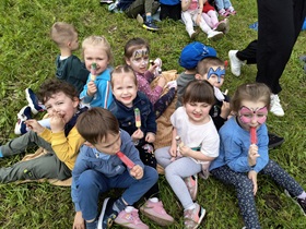 Dziesięcioro dzieci siedzą na kocu, uśmiechają się do zdjęcia, w rękach trzymają lody. Troje dzieci ma pomalowane twarze.