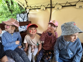 3 dziewczynki i chłopiec siedzą w wozie. Dziewczynki mają pomalowane twarze w jednorożca, motylki oraz myszkę Miki. Jedna z dziewczynek pokazuje z palców serce.