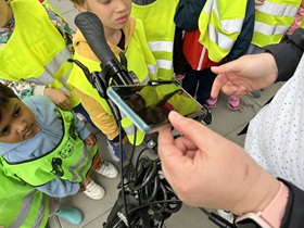 Dzieci zebrane wokół pani patrzą jak w uchwycie umocowany jest telefon.