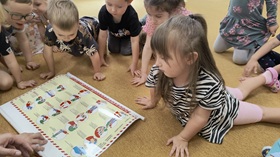 Dzieci siedzą na dywanie i oglądają planszę, przedstawiającą zasady udzielania pierwszej pomocy.