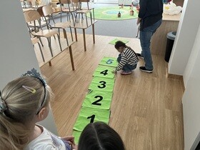 Dziewczynka w bluzce w paski ukucnęła przy kwadracie z cyfrą 5.