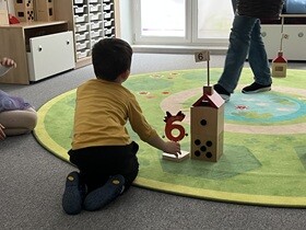 Chłopiec ustawia obok drewnianego domku cyfrę 6.