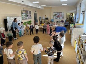 Dzieci stoją w kole i naśladują ruchy wykonywane przez panią.