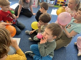 Dzieci siedzą na dywanie i nadmuchują balony.