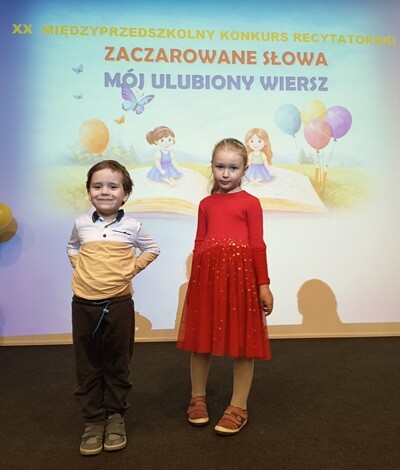 Chłopiec i dziewczynka stoją na scenie. Za nimi wyświetlony jest napis XX Międzyprzedszkolny Konkurs Recytatorski „Zaczarowane słowa – mój ulubiony wiersz”.