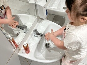 Przed umywalką stoi dziewczynka, która myje wierzchnią część dłoni.