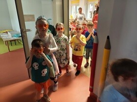 Dzieci wychodzą z sali jedno za drugim. Kazde dziecko ma pomarańczowe okulary na oczach.